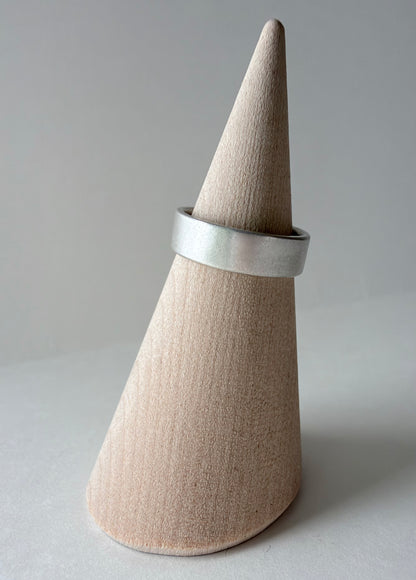 A wide, square, matte silver ring band displayed on a wood cone stand against a neutral gray background.