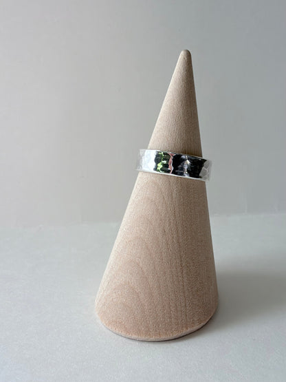 A polished thick silver hammered ring band displayed on a wooden cone stand against a soft gray background.