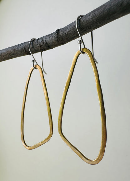 Brass wing shaped hoop earrings hanging on a branch against a neutral background
