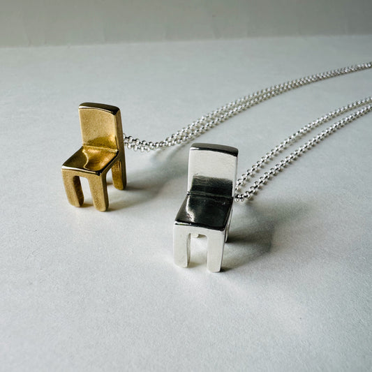 Brass and silver chair-shaped pendants on chains against a light gray background