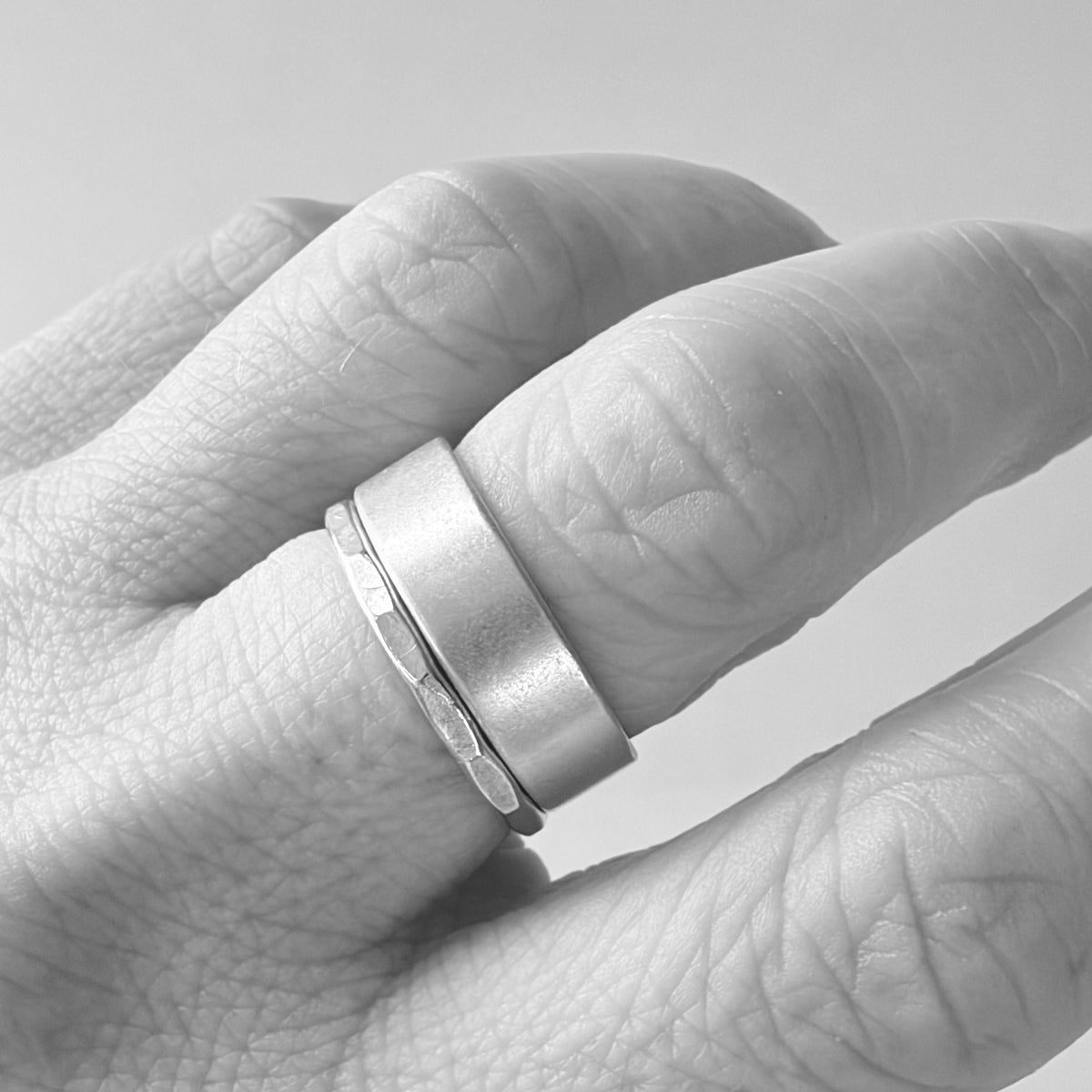 A close-up of a hand wearing a minimalist silver ring with a matte finish and a textured band.