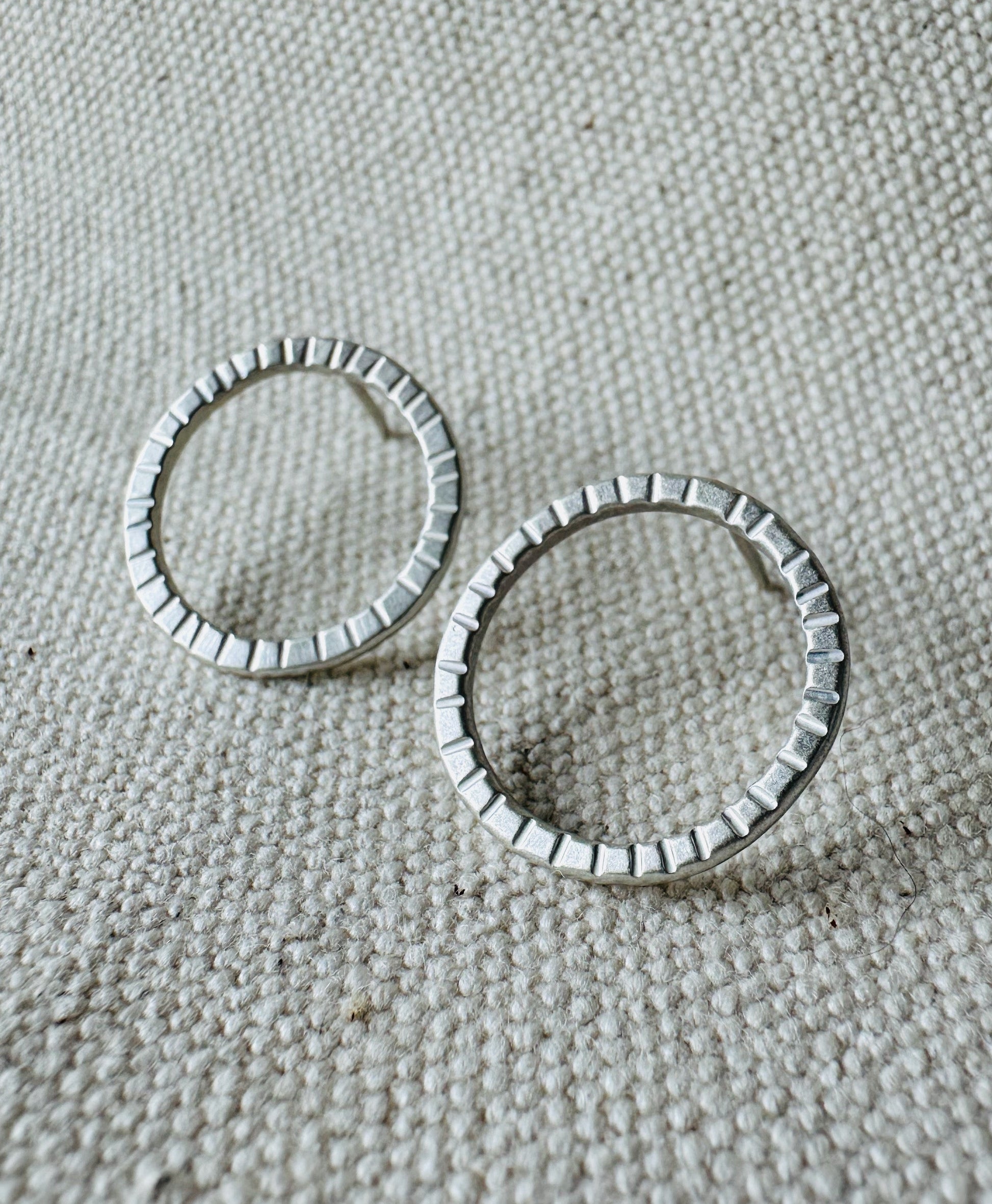 Close up image of silver (2 cm) open circle stud earrings with hand stamped tracks texture. 