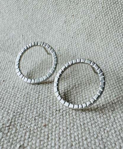 Close up image of silver (2 cm) open circle stud earrings with hand stamped tracks texture. 