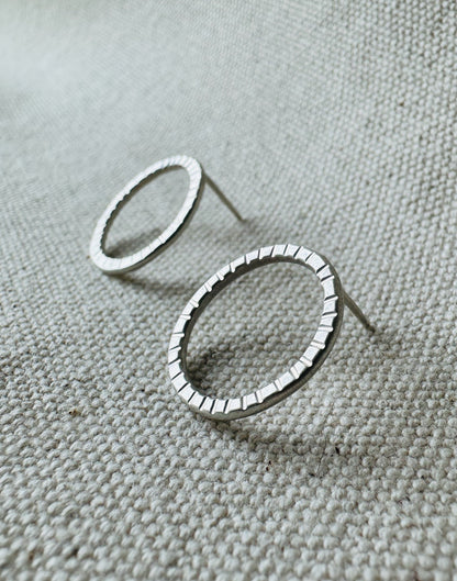 Close up image of silver (2 cm) open circle stud earrings with hand stamped tracks texture. 