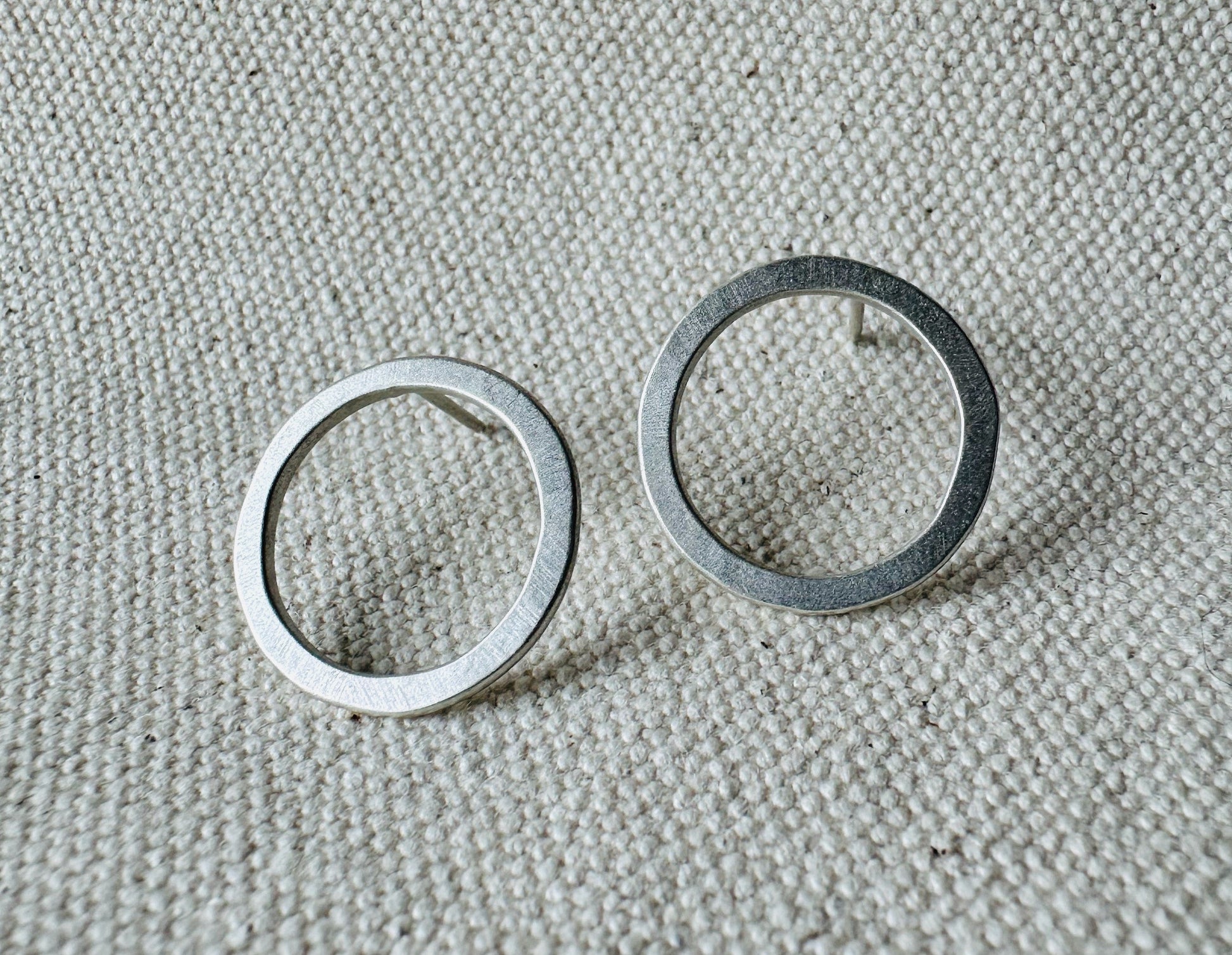 Close up image of silver (2 cm) open circle stud earrings with satin texture. 