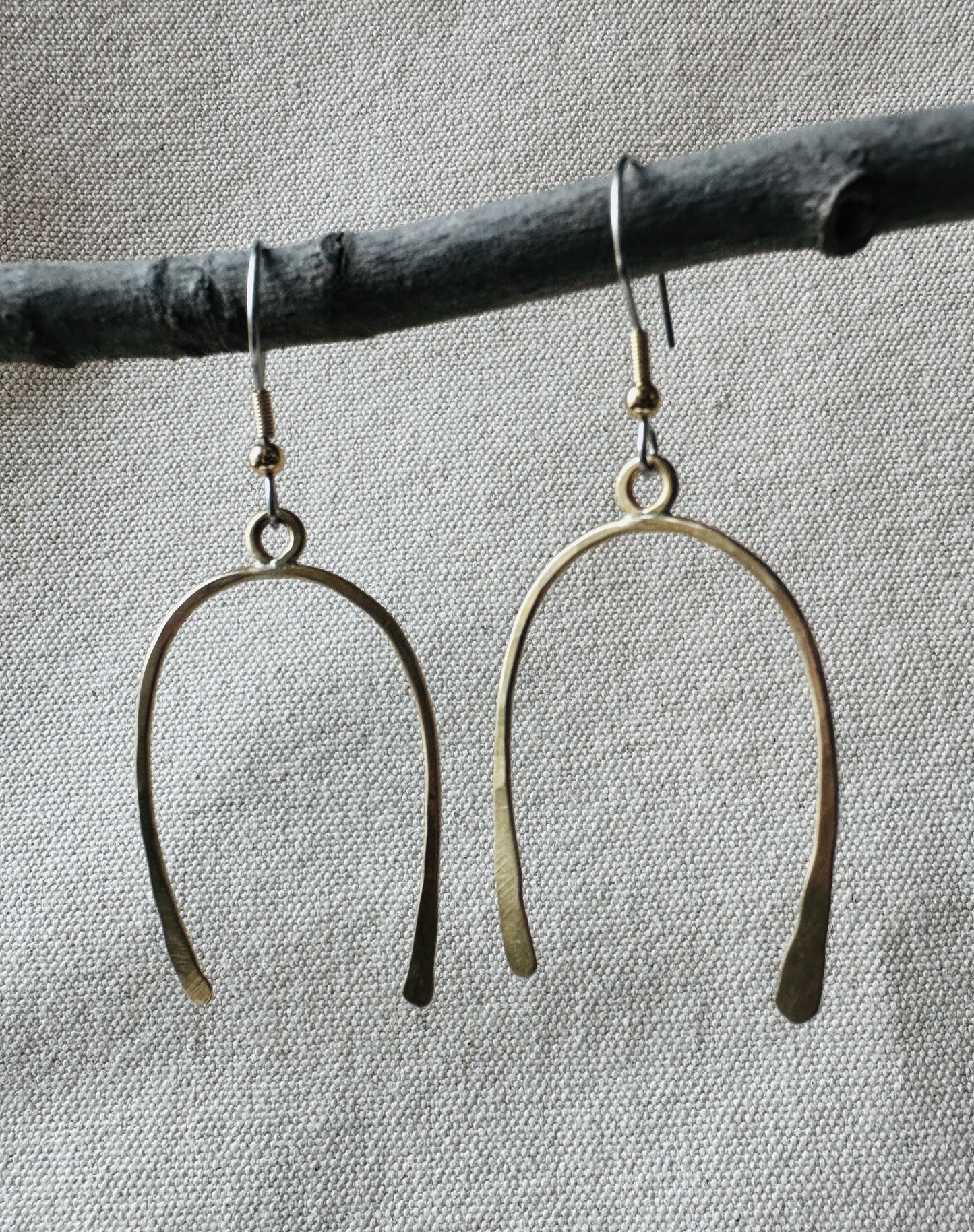 Close up image of brass arch shaped dangle earrings on small branch.