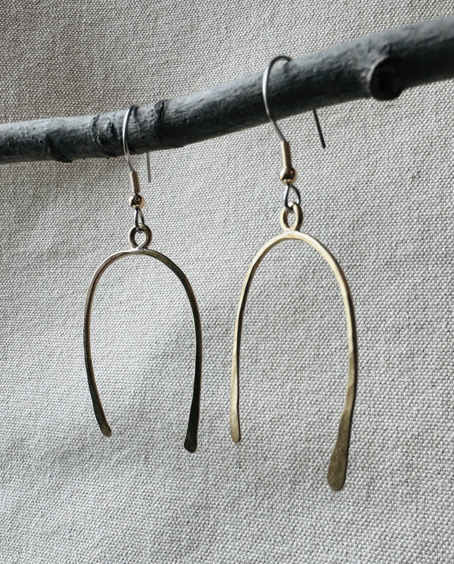 Close up image of brass arch shaped dangle earrings on small branch.