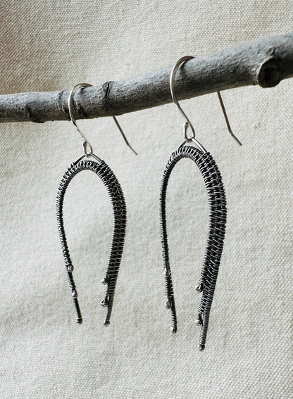 Close up image of sterling silver wire wrapped rainbow dangle earrings on small branch. 