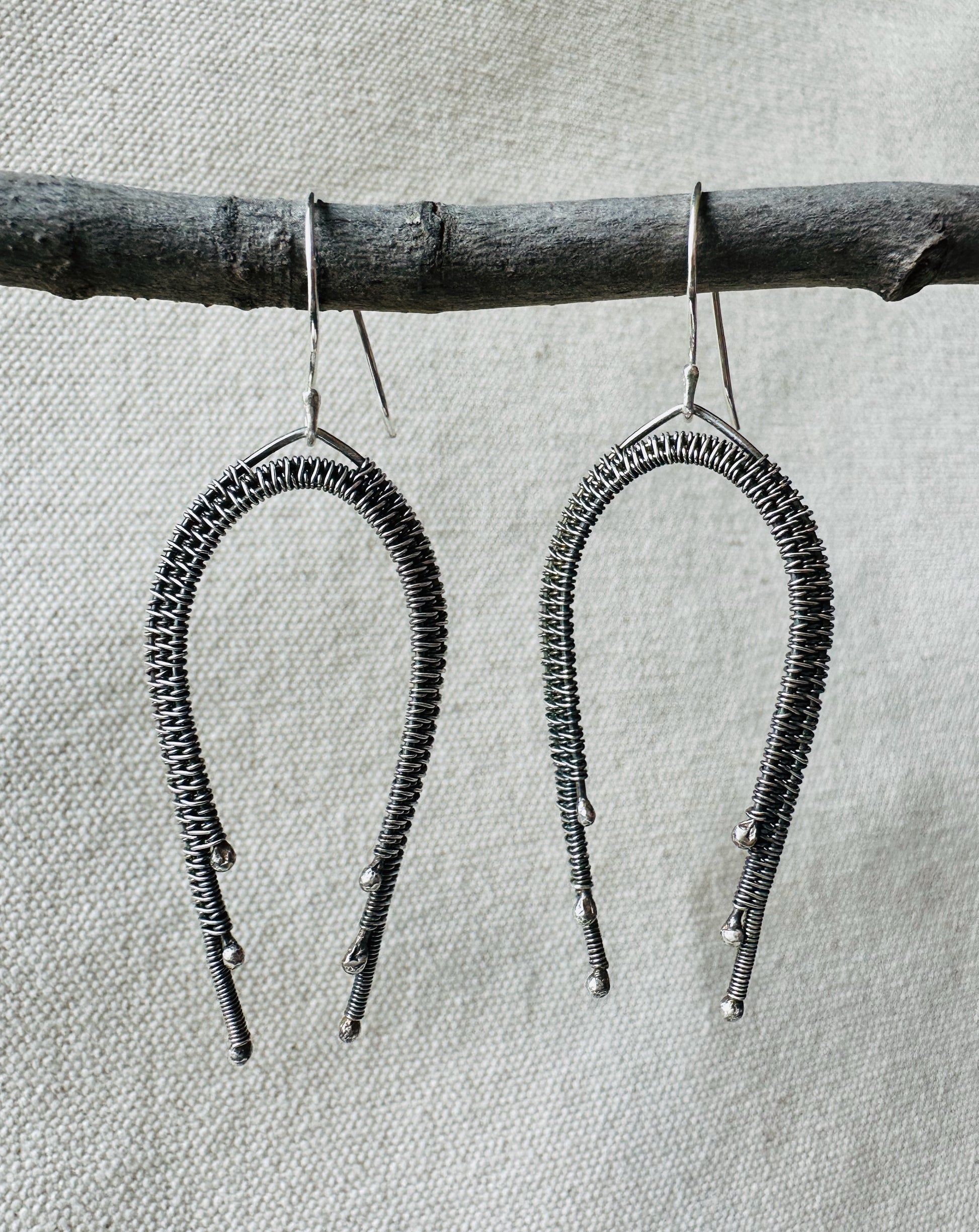 Close up image of sterling silver wire wrapped rainbow dangle earrings on small branch. 