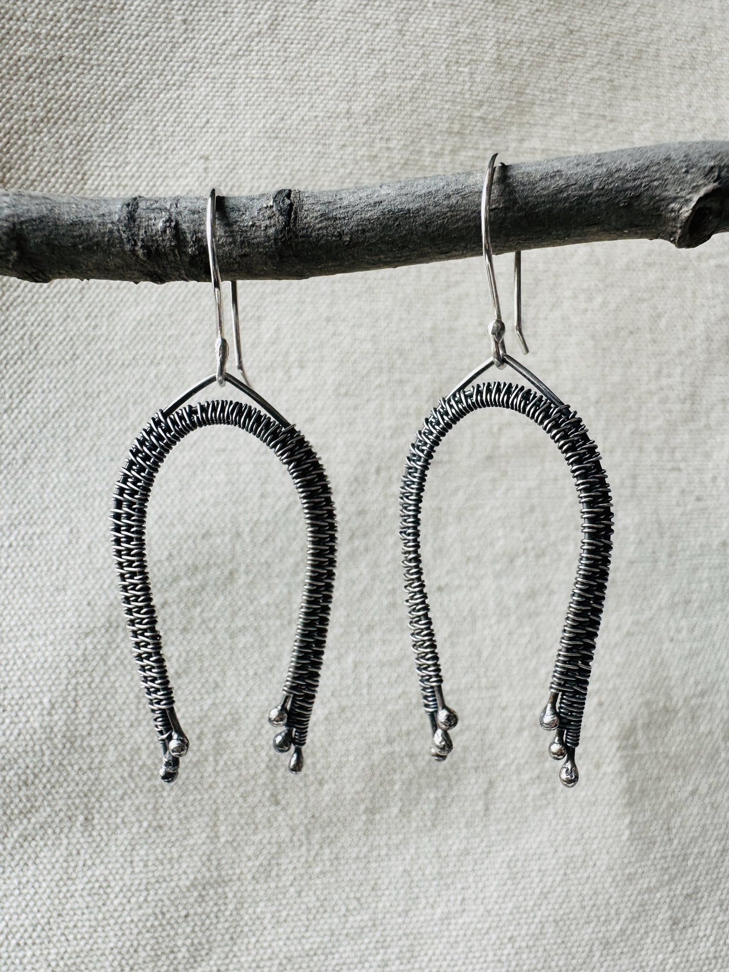 Close up image of sterling silver wire wrapped rainbow dangle earrings on small branch. 