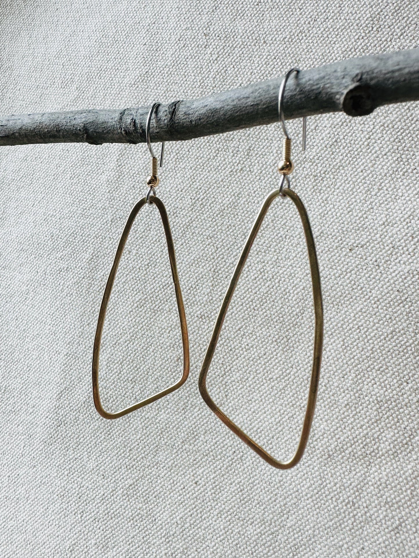 Close up image of brass wing shaped dangle earrings on small branch. 