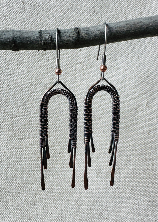 Close up image of copper wire wrapped rainbow dangle earrings on small branch. 