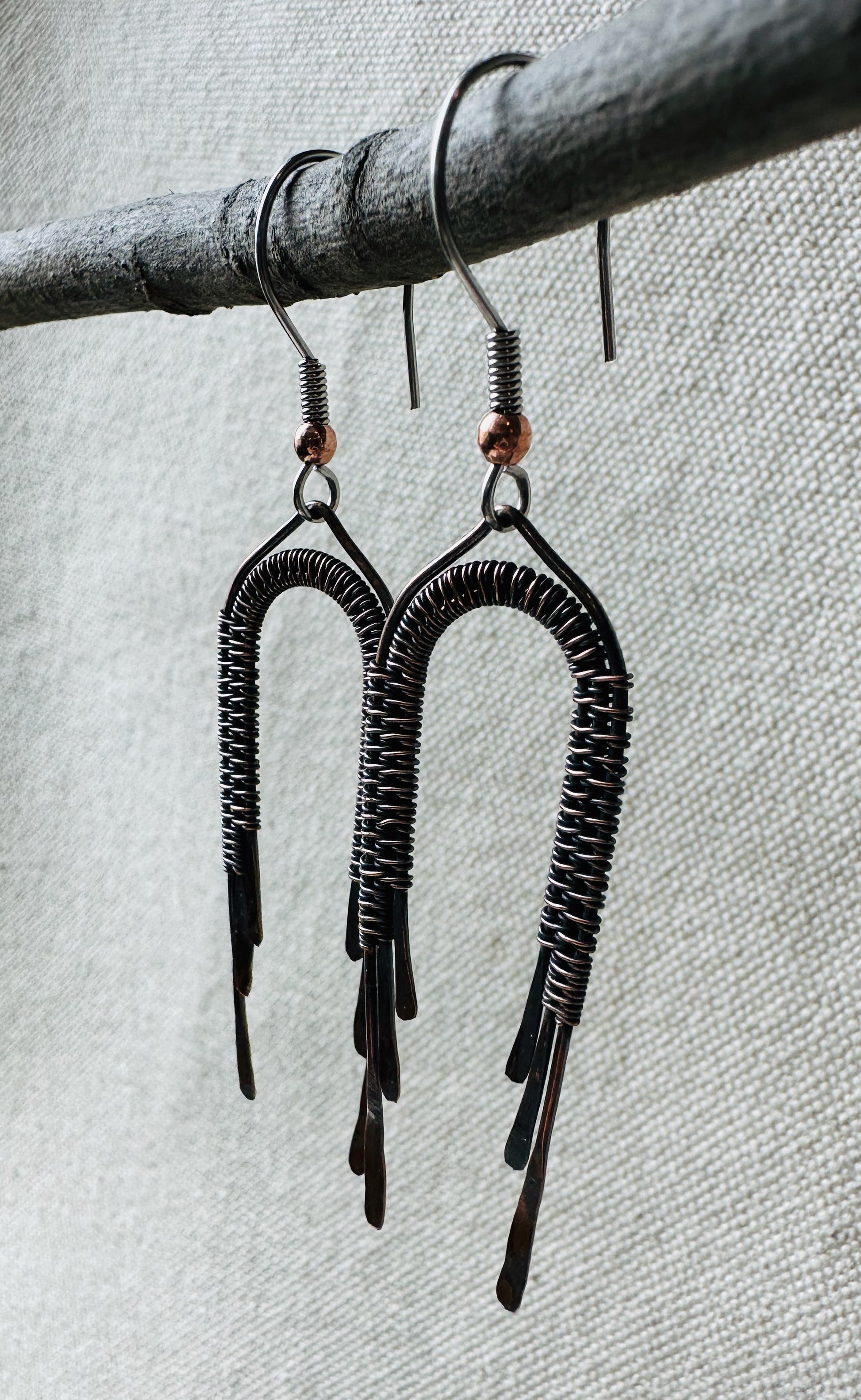 Close up image of copper wire wrapped rainbow dangle earrings on small branch. 