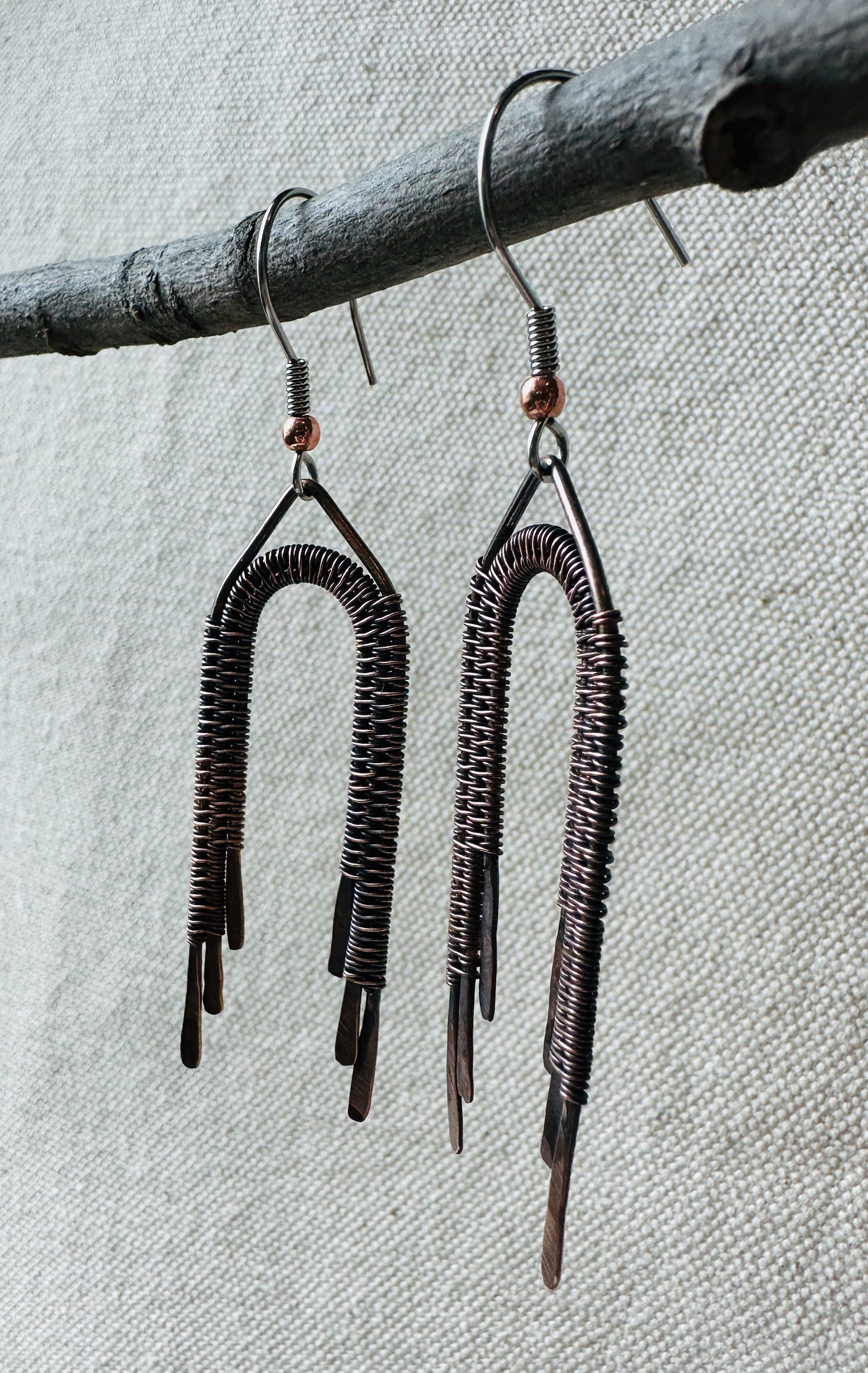 Close up image of copper wire wrapped rainbow dangle earrings on small branch. 