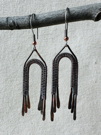 Close up image of copper wire wrapped rainbow dangle earrings on small branch. 