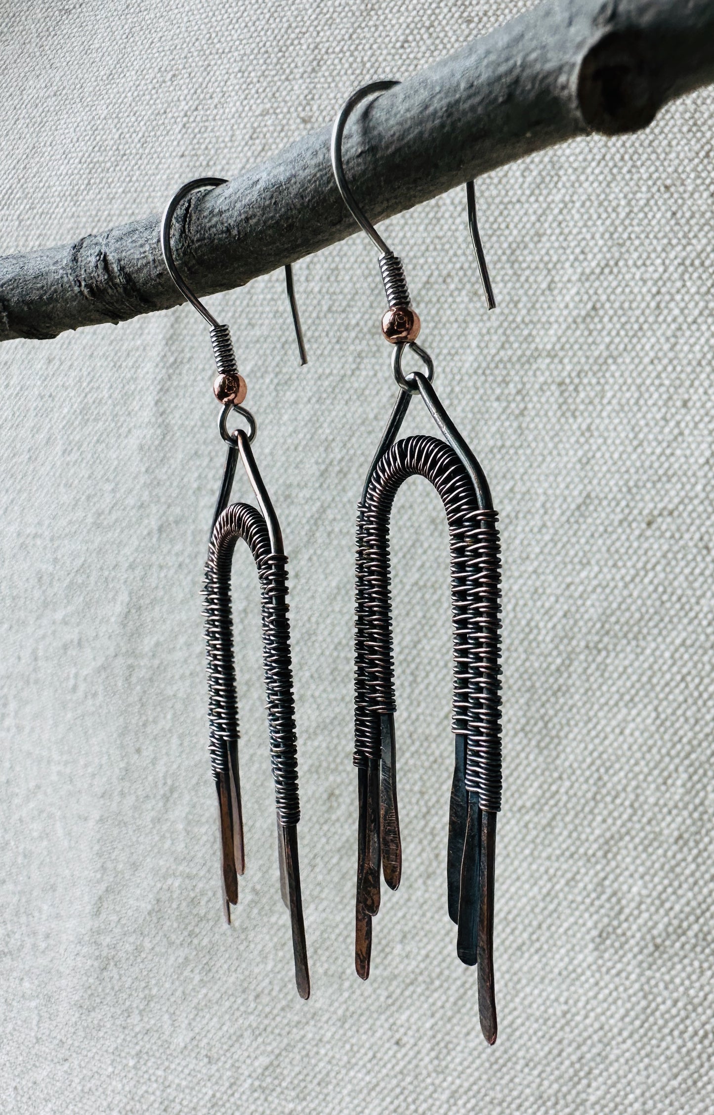 Close up image of copper wire wrapped rainbow dangle earrings on small branch. 