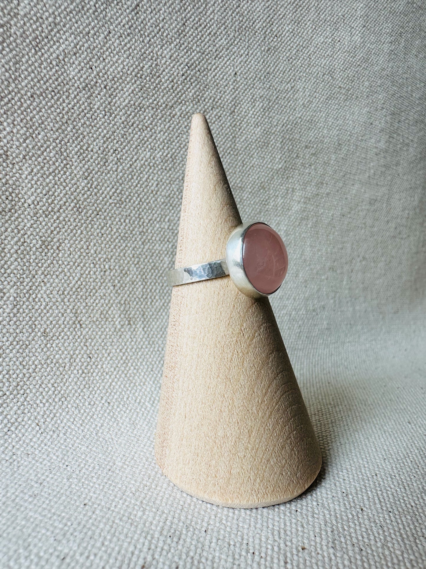 Silver rose quartz gemstone ring with hammered ring band on wooden ring holder.  