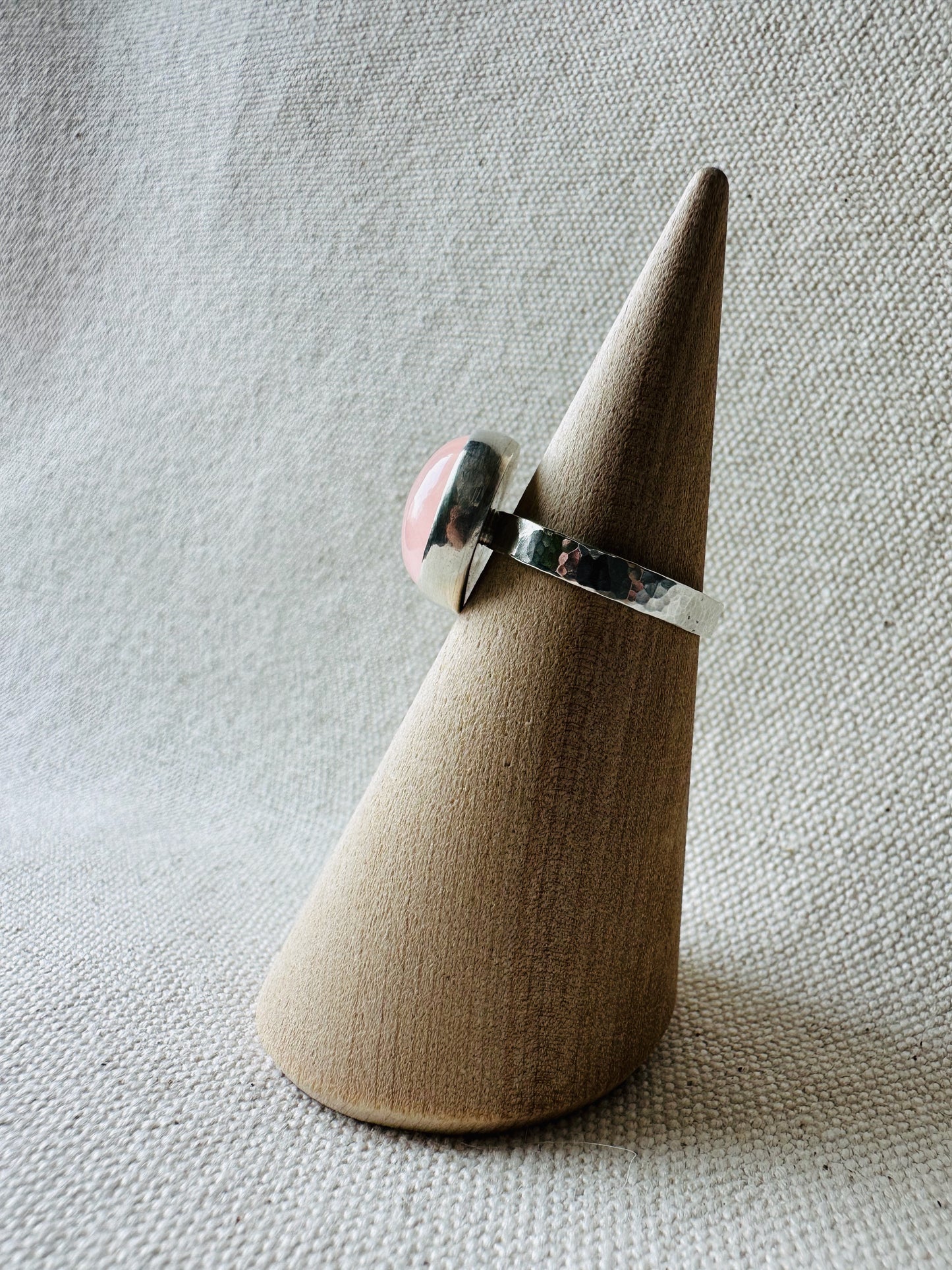 Silver rose quartz gemstone ring with hammered ring band on wooden ring holder.  