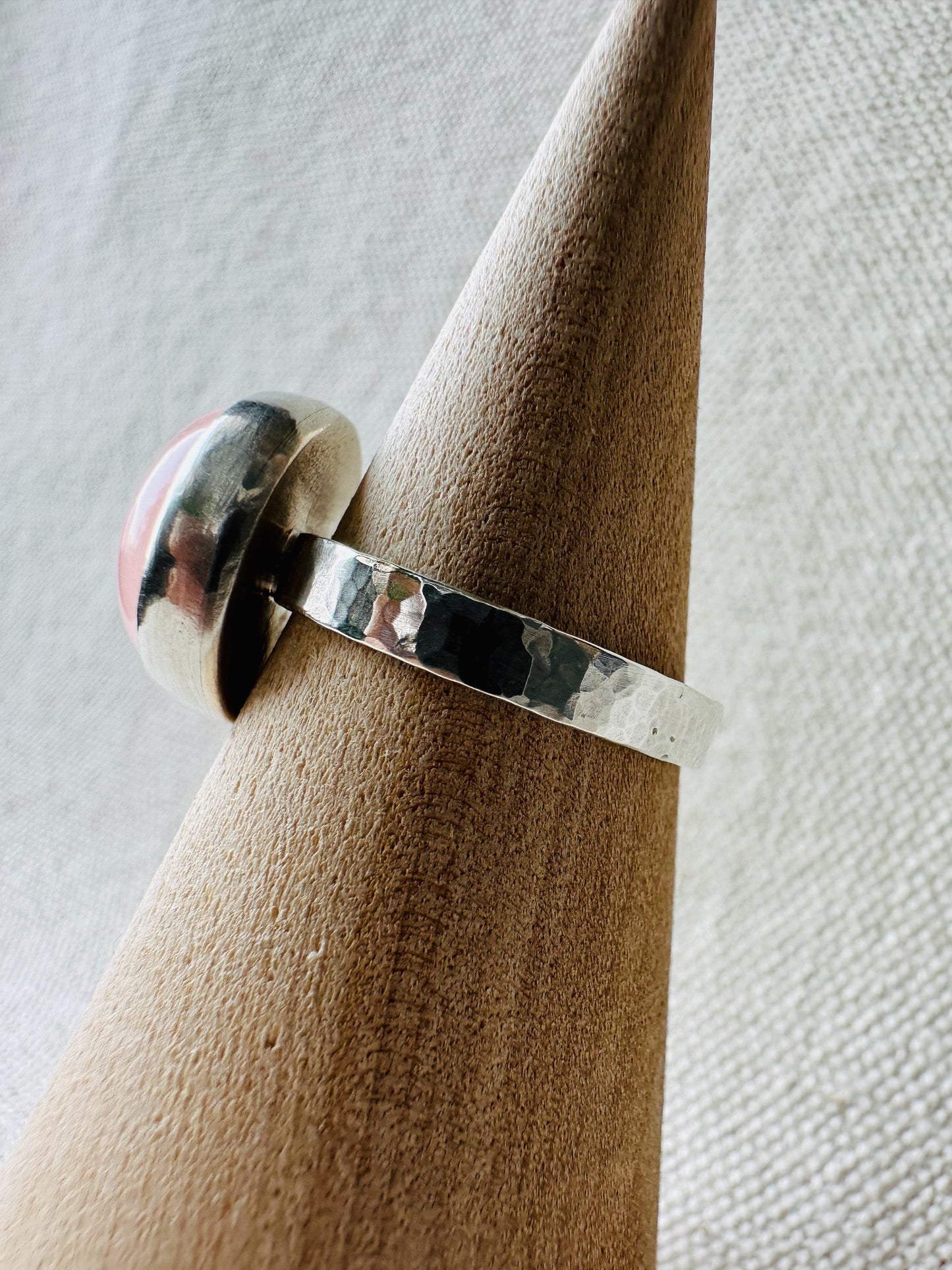 Close up side view of silver rose quartz gemstone ring with hammered ring band on wooden ring holder.  