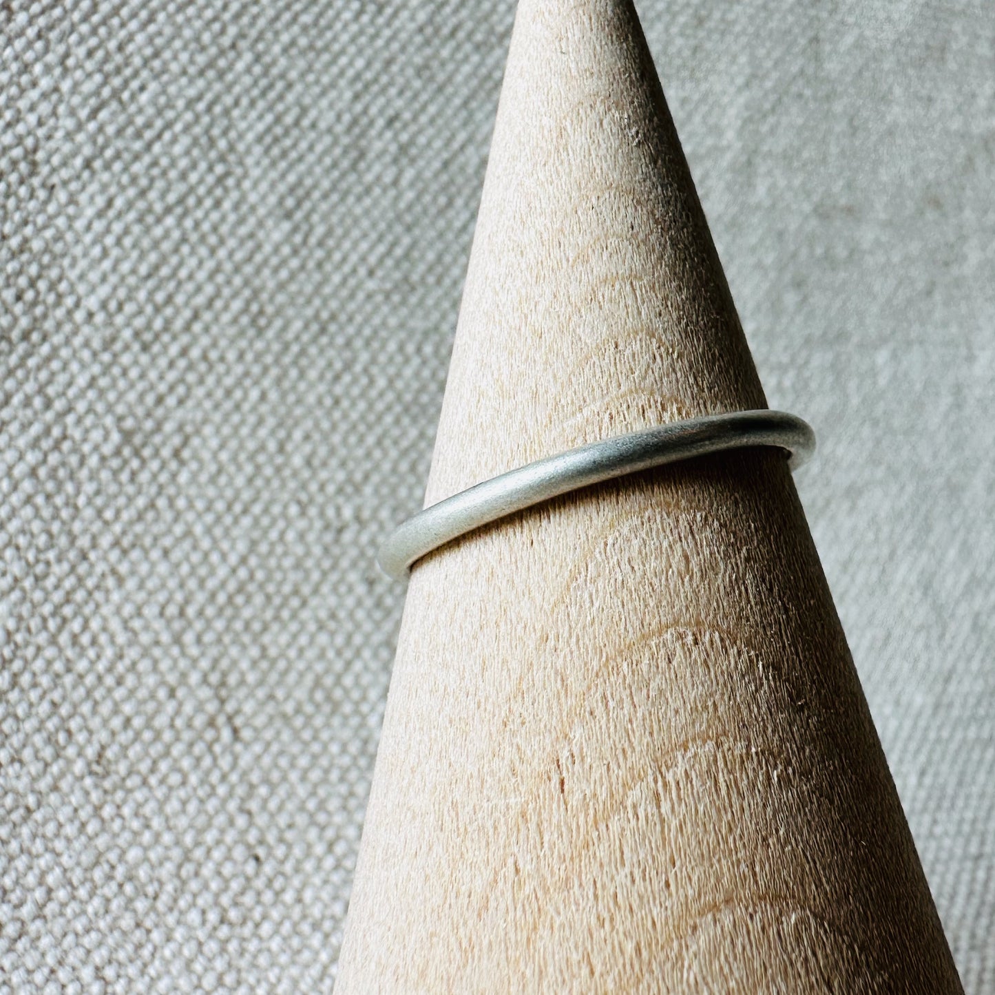 Closeup image of round silver ring on wooden ring holder. 