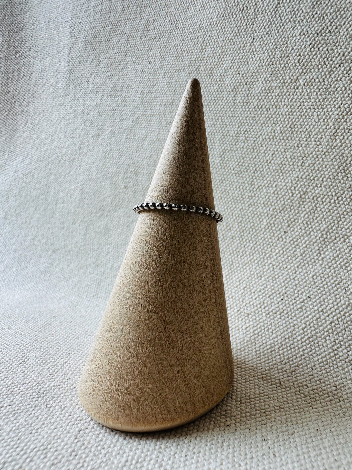 Beaded wire silver ring on wooden ring holder. 