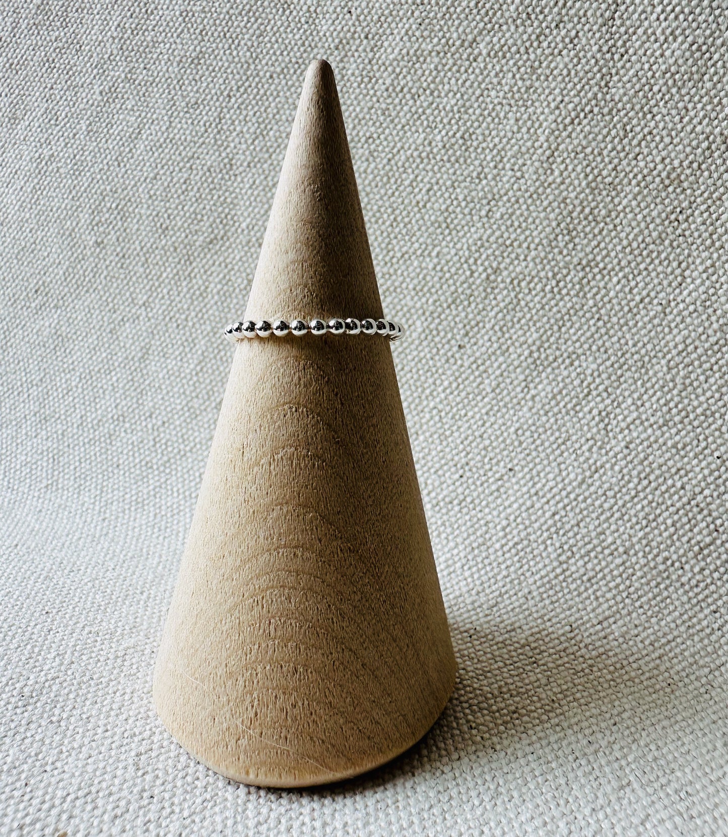 Beaded wire silver ring on wooden ring holder. 