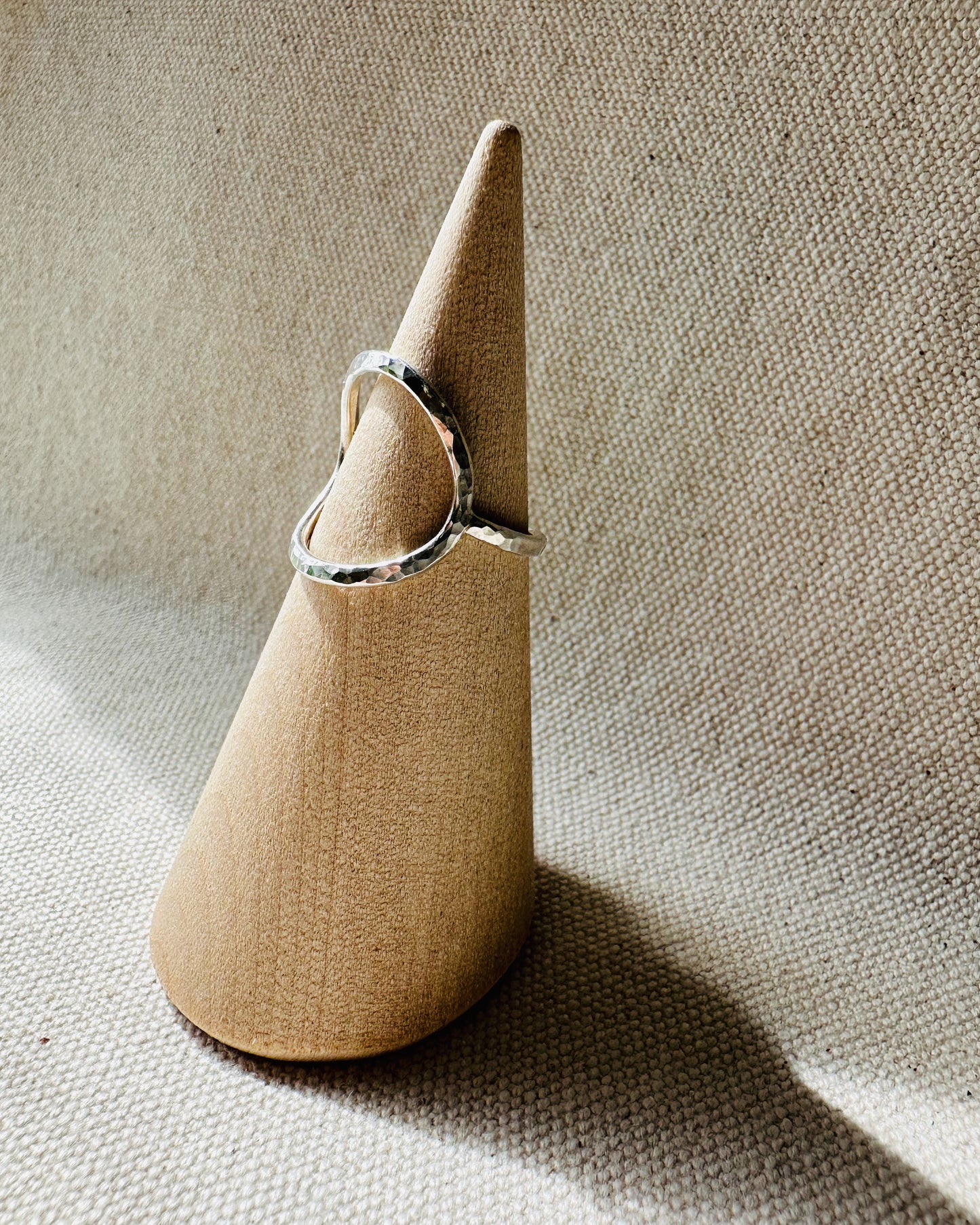 Open circle silver ring with hammered finish on a wooden ring holder. 