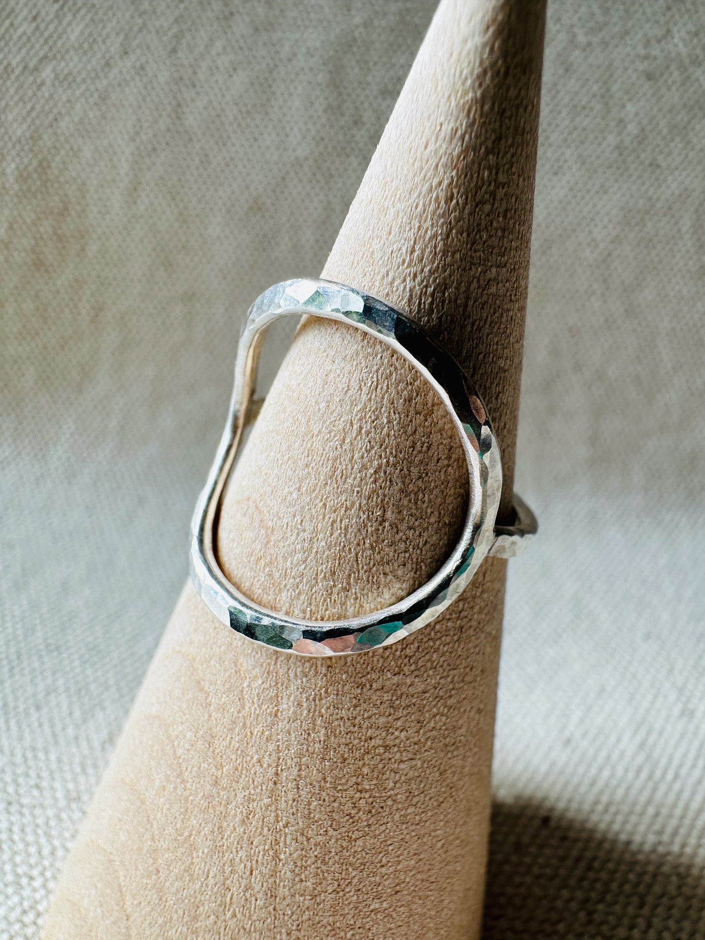 Close up image of open circle silver ring with hammered finish on a wooden ring holder. 