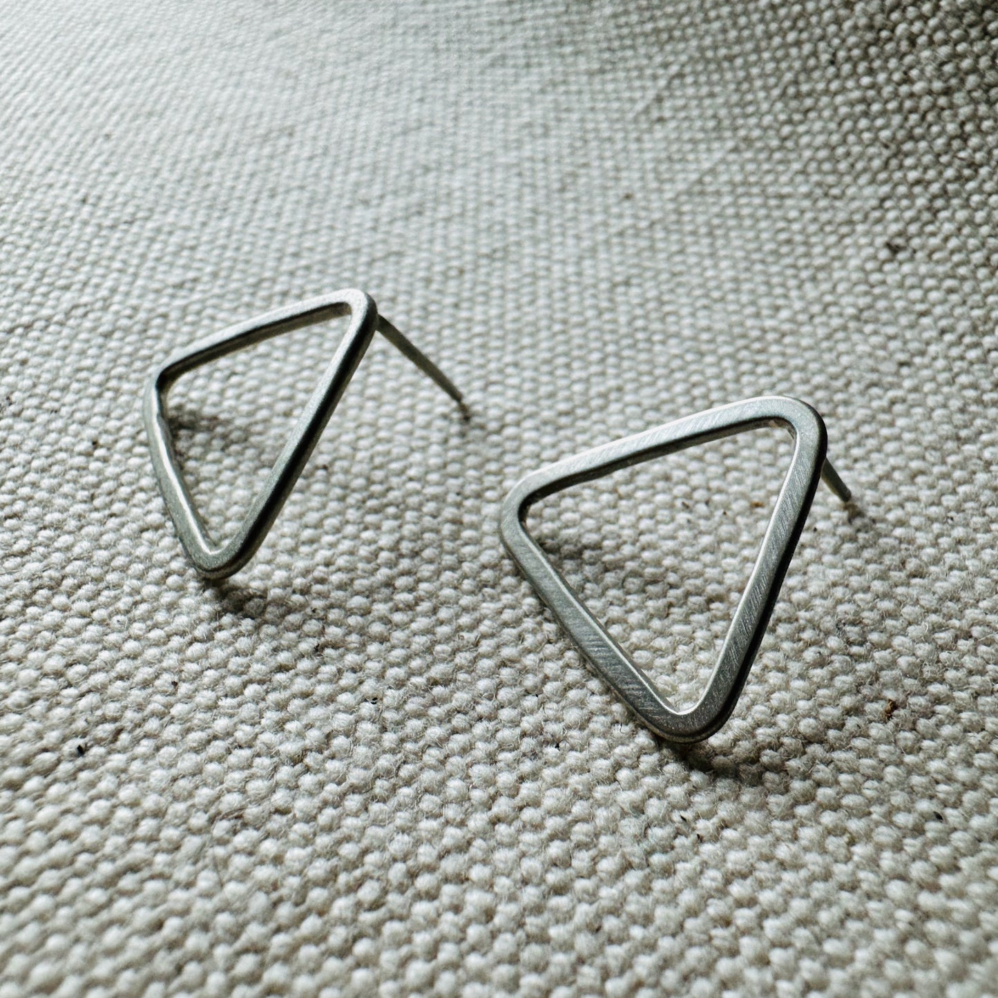 Close-up image of silver satin triangle stud earrings, approximate size (2 cm).