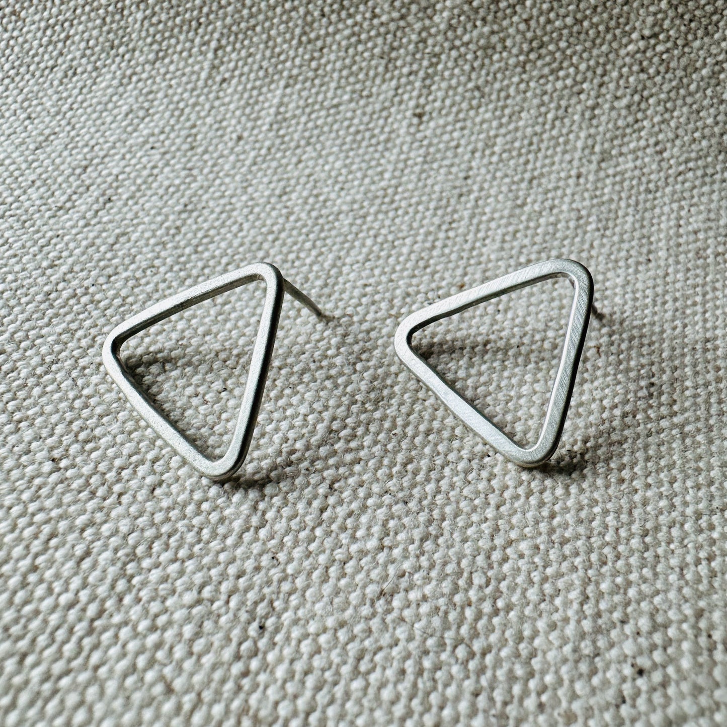 Close-up image of silver satin triangle stud earrings, approximate size (2 cm).