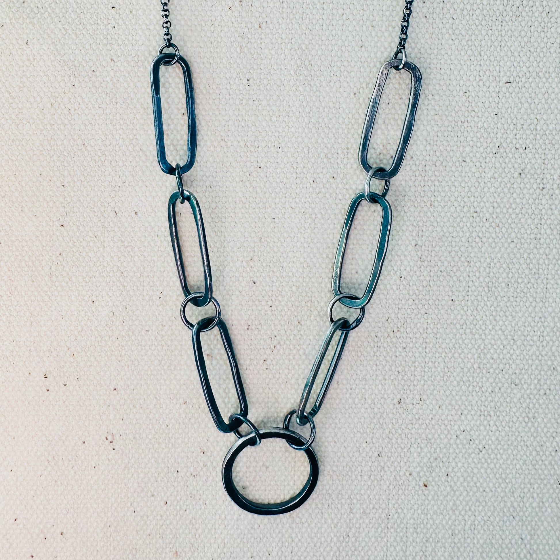 Close up image of hand fabricated, oxidized sterling silver, single circle and 6 paperclip link chain necklace.