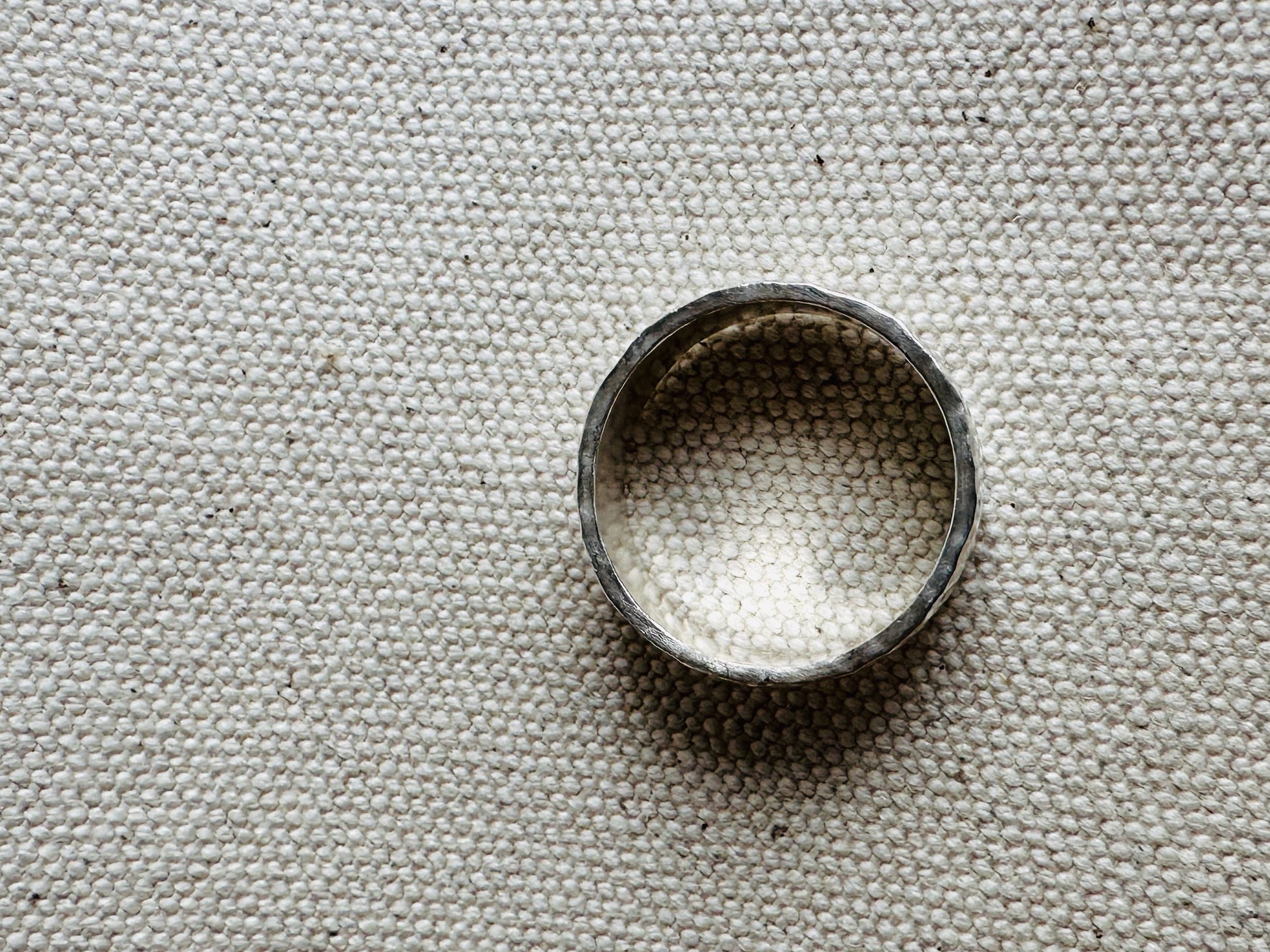 Hammered thick band silver ring laying on side. 