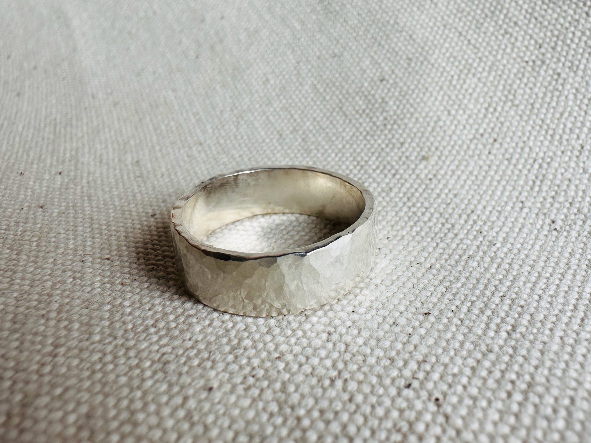 Hammered thick band silver ring laying on side. 