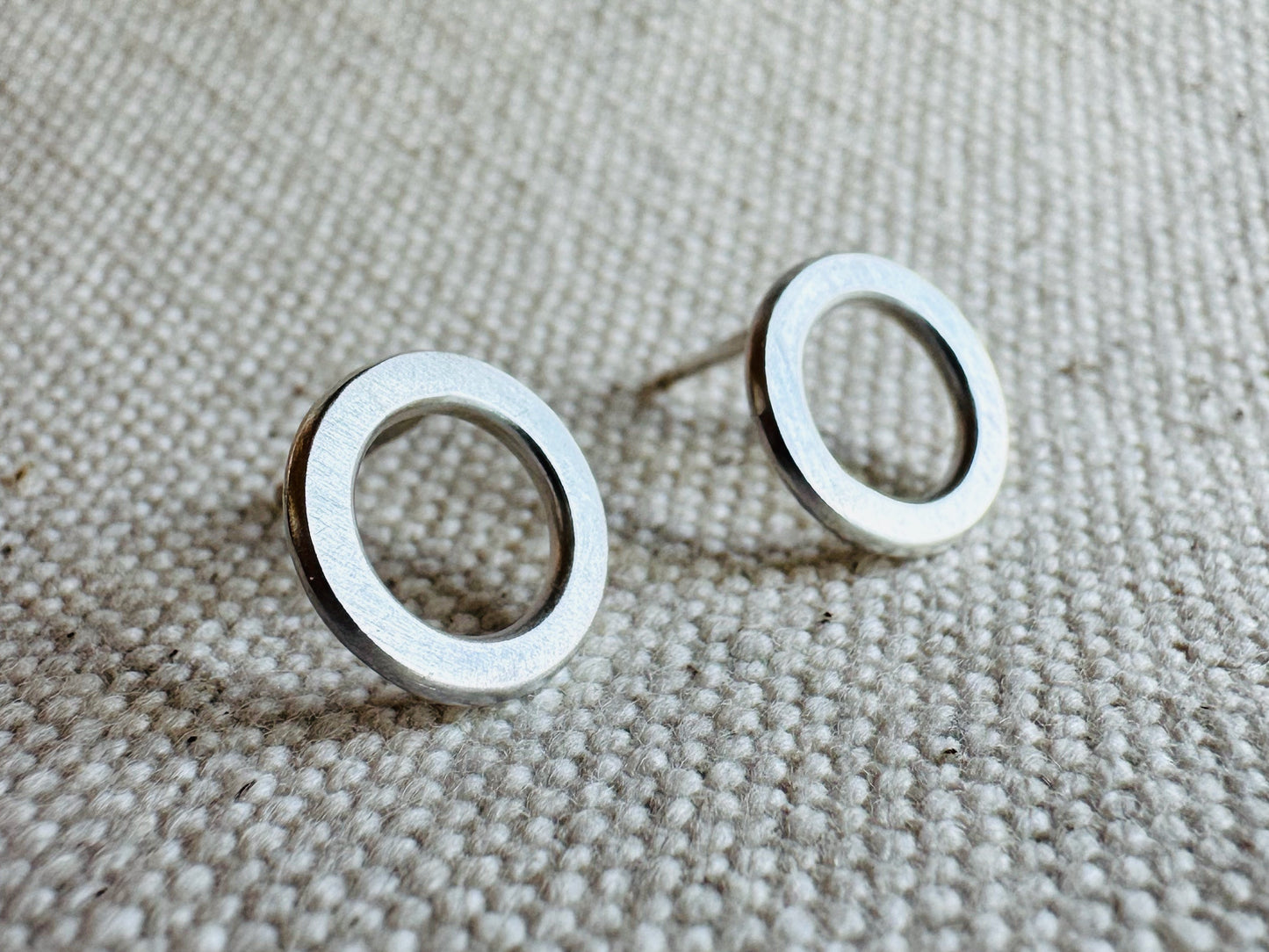 Close up image of silver (1 cm) open circle stud earrings with satin texture.