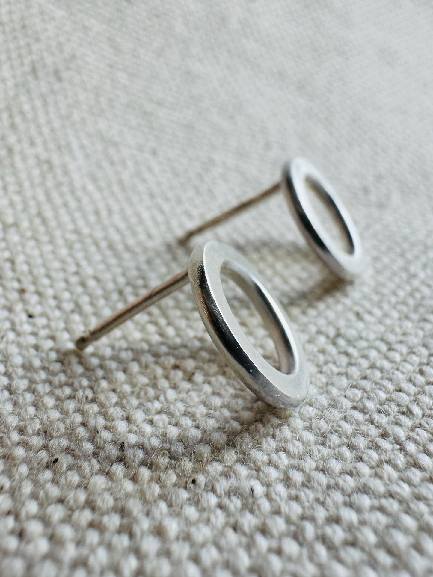 Close up image side angle view of silver (1 cm) open circle stud earrings with satin texture.