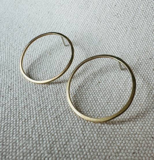 Close up image of brass (3 cm) open circle stud earrings with satin texture. 