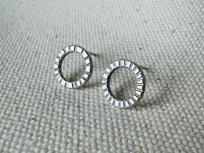 Close up image of silver (1 cm) open circle stud earrings with hand stamped tracks texture.