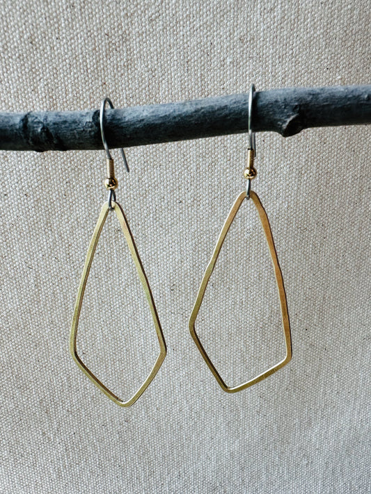 Close up image of brass geometric shaped dangle earrings on small branch.