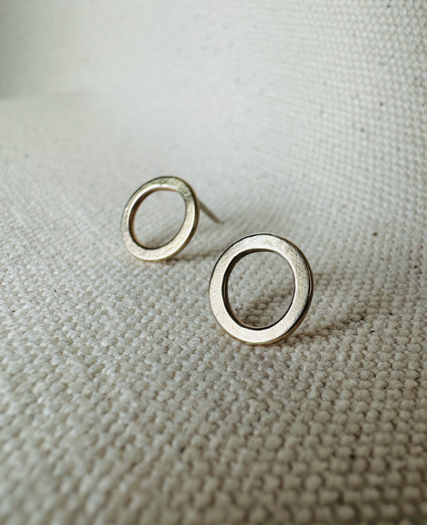 Close up image of brass (1 cm) open circle stud earrings with satin texture. 