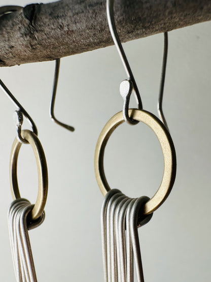 Close-up view of pair of brass circle dangle earrings with silver fringe and silver ear wires with satin finish.