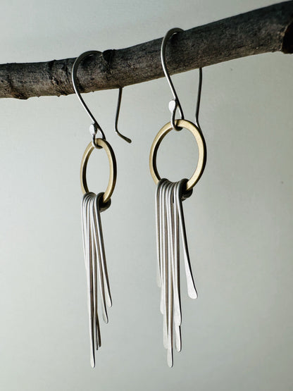 Side view of a pair of brass circle dangle earrings with silver fringe and silver ear wires with satin finish.