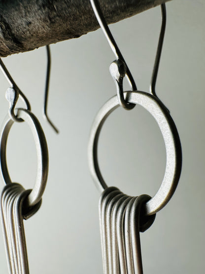 Close-up view of pair of silver circle dangle earrings with fringe with satin finish.