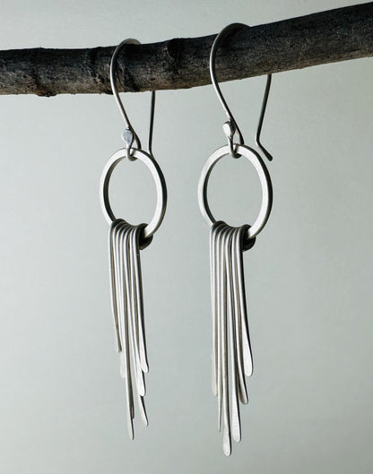 Side view of pair of silver circle dangle earrings with fringe with satin finish.