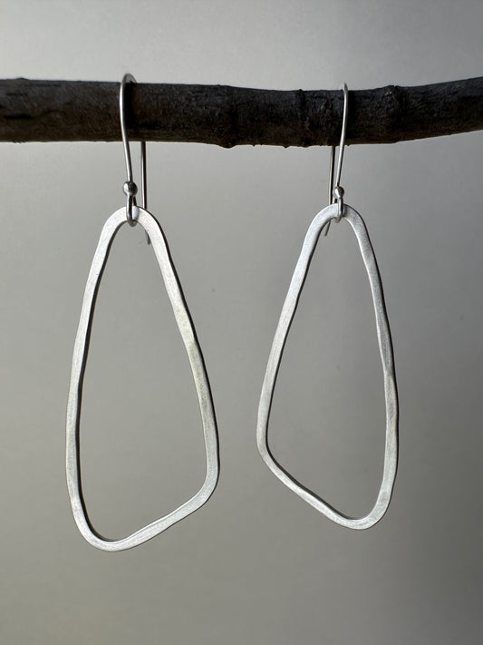 Pair of silver wing shaped hoop earrings hanging on a branch against a gray background