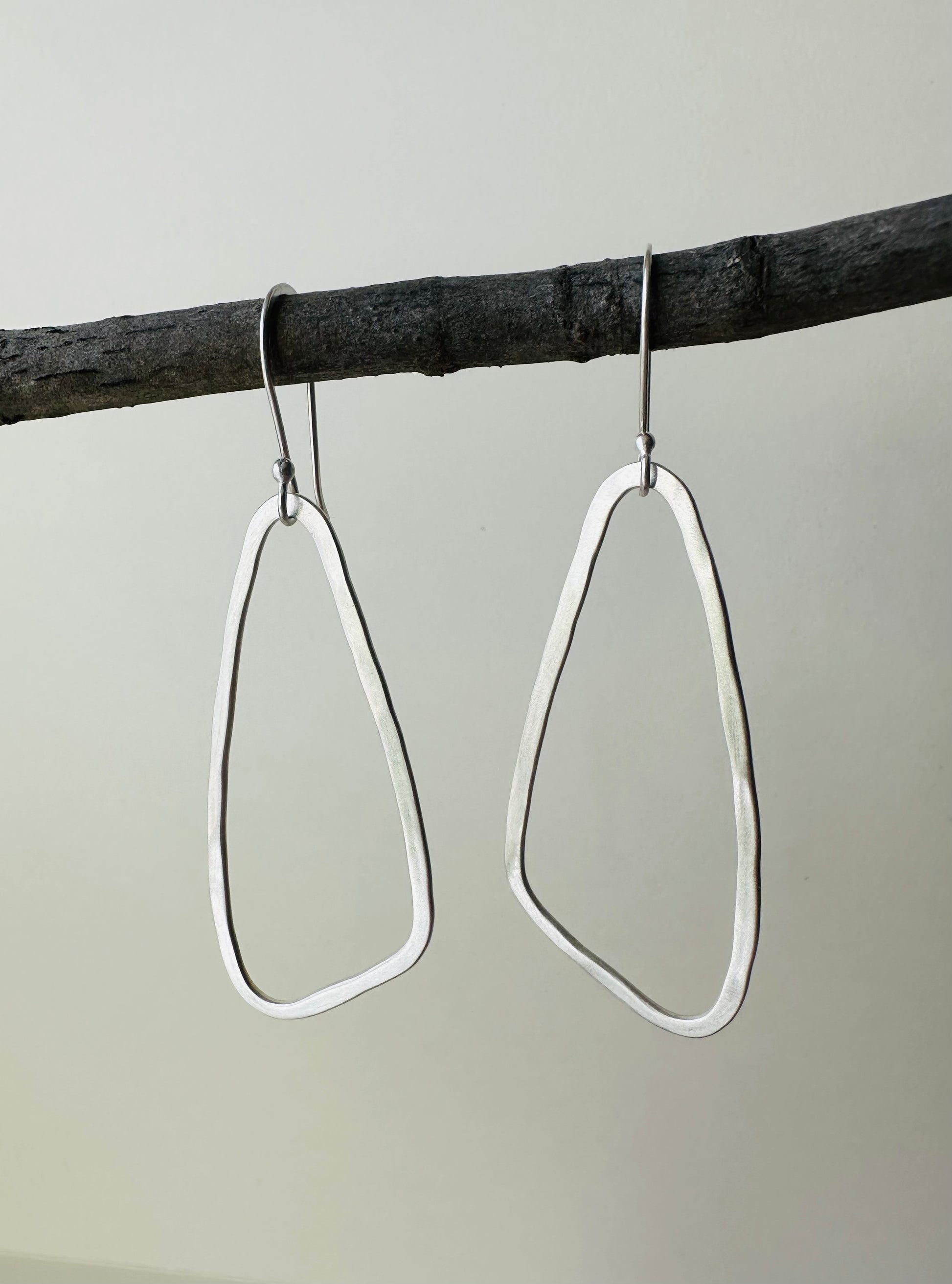 Pair of silver wing shaped hoop earrings hanging on a branch against a gray background