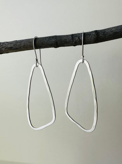 Pair of silver wing shaped hoop earrings hanging on a branch against a gray background