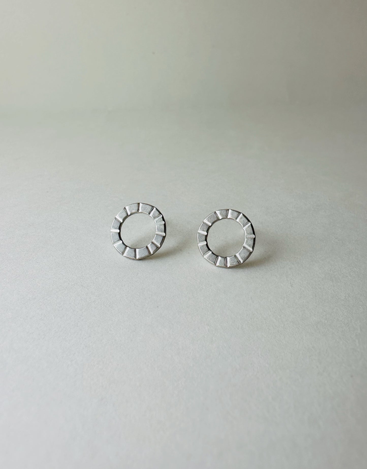 Pair of silver circle earrings with hand stamped lines on a light gray background
