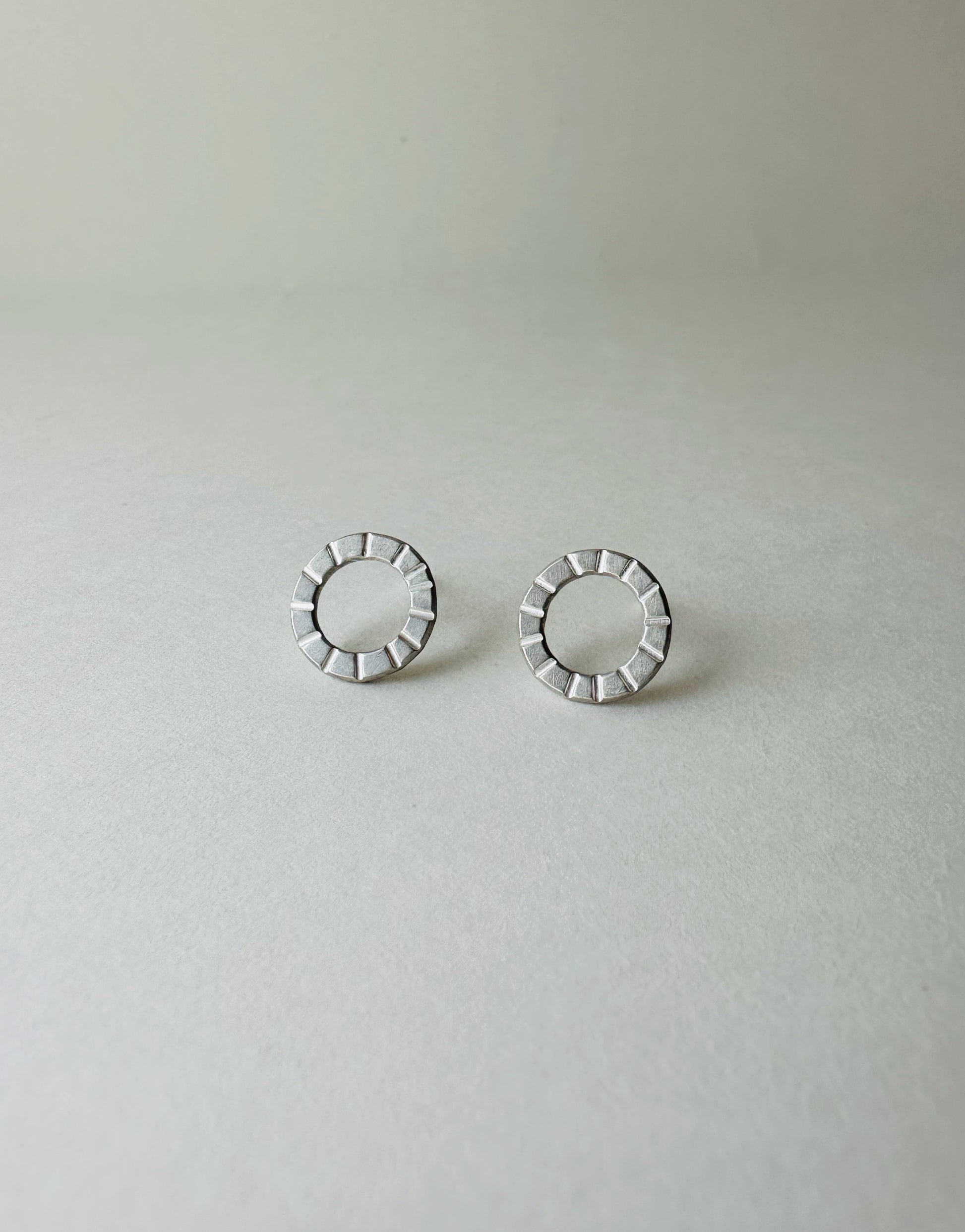 Pair of silver circle earrings with hand stamped lines on a light gray background