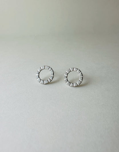 Pair of silver circle earrings with hand stamped lines on a light gray background