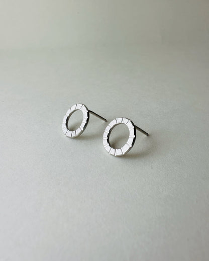 Pair of silver circle earrings with hand stamped lines on a light gray background